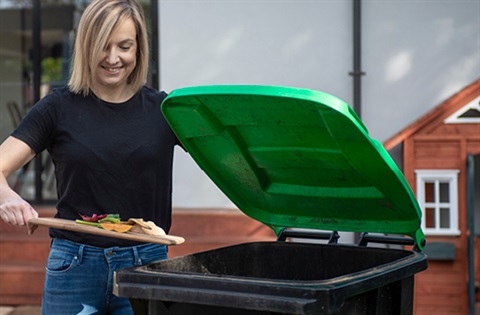woman in garden putting garden waste in green bin