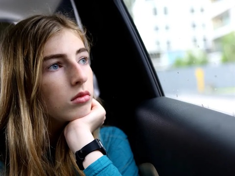 Georgie Stone seated inside a car, resting their chin on their hand and looking out through the window.