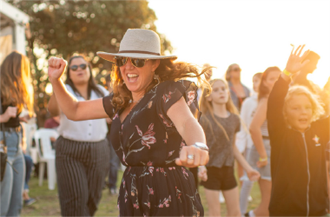 A woman laughing and dancing with her arms out at dusk in a crowd of people.