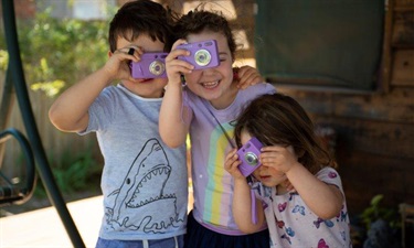 Children playing with toy cameras and laughing in backyard at family day care