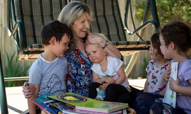 Woman smiling with children as she reads from a book in her homeime with