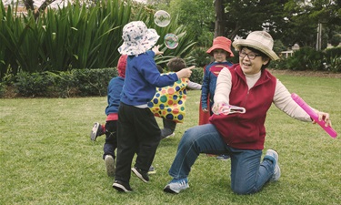 Woman plays with children blowing bubbles and running through the park