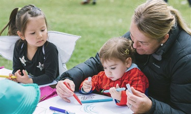 Little girl with fairy wings looks on as her friend does some colouring in