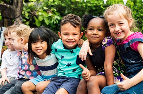 A group of 6 young children huddled together and smiling at the camera