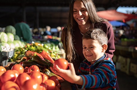 A young boy and his mother looking at tomatoes in a row of vegetables at the market