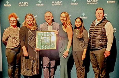 A group of 6 Kingston staff, with one in the centre holding the framed MAV Award