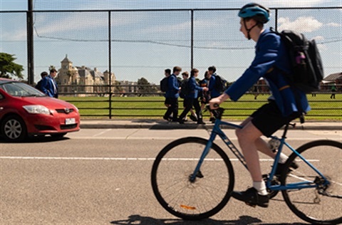 A high school student riding their bike along the road outside their school