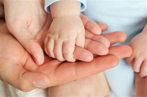 A babies hand being cupped by one hand from each of their parents