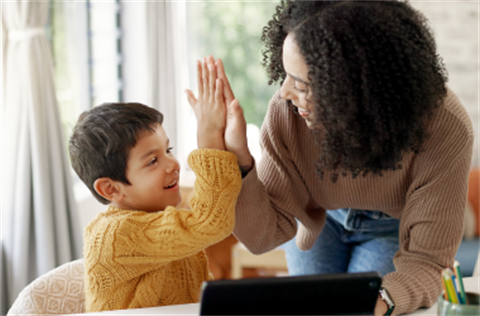 A female care giver high-fiving a young boy