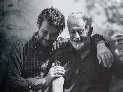 one younger man and one older man stnading side by side and smiling. the young man has his arm around the older man's shoulders.
