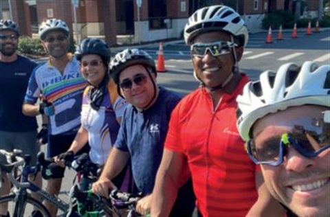 A line of people on their bicycles wearing helmets and sunglasses and smiling to camera
