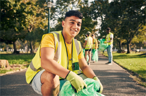 A young person dressed in high vis, wearing gloves and holding a pale green garbage bag.