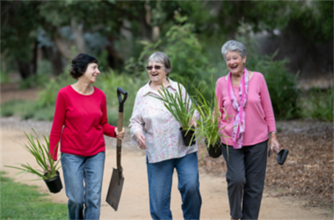3 women carrying plants and shovels at a park