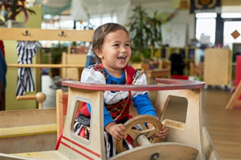 A young child driving a wooden toy car at a childcare centre