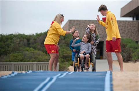 Lifeguards and kids share a high five at the top of a beach access mat.