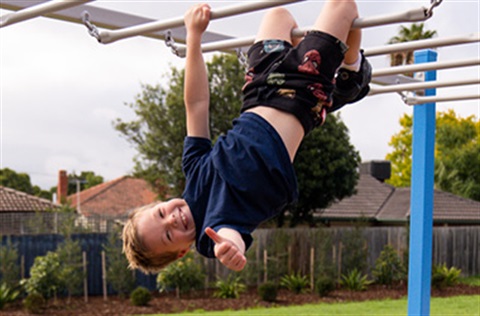 Child giving a thumbs up while hanging upside-down from monkey bars