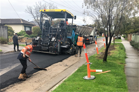 A large truck in the middle of the road with two tradesman wearing high vis resurfacing a road.