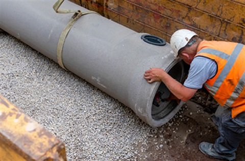 A construction worker assessing a large drainage pipe