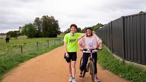 A walker and a cyclist pose for a photo on a shared walking and biking trail