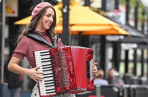 Woman in a beret playing an accordion on a street near a cafe